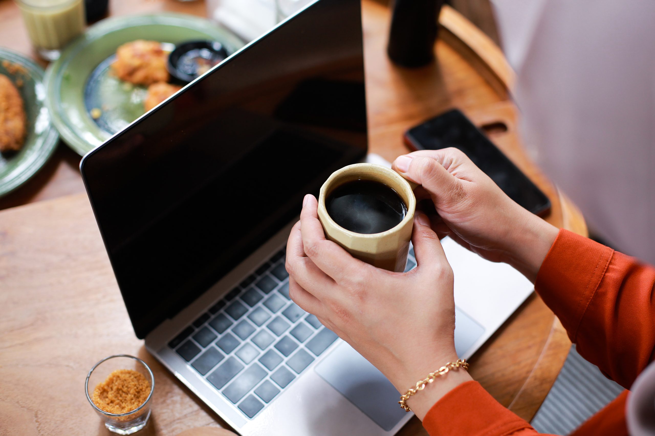 woman-hands-holding-cup-coffee-while-working-with-laptop-cafe